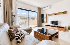 Un salon moderne avec un canapé, une table basse, un téléviseur et un balcon offrant une vue agréable.