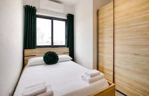 Ein Hotelzimmer mit einem Bett, einem Fenster mit Vorhängen, einem Holzschrank und einem grünen Zierkissen.