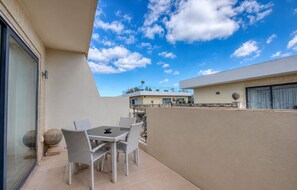 Eine Terrasse im Freien mit Tisch und Stühlen, einer Glastür und Blick auf ein Gebäude mit Balkon.