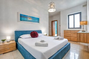 Une chambre à coucher avec un grand lit, une table de chevet avec une lampe, une commode et un tableau accroché au mur.