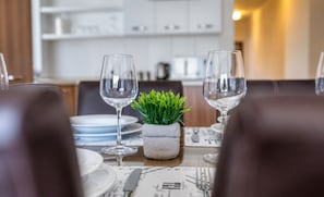 Une table à manger dressée avec des assiettes, des couverts et deux verres à vin, et une petite plante en pot placée au centre.