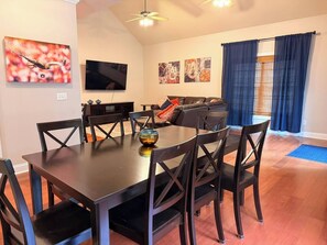 A dining area with a table and chairs, a television, artwork on the walls, and a view of the living room. - Spacious 3 Bed 3 Bath Tiger Den – 1 Mile to AU! (Auburn)