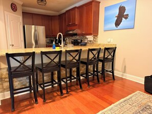 A kitchen with a granite countertop, stainless steel appliances, wooden cabinets, and a bar area with four chairs. - Spacious 3 Bed 3 Bath Tiger Den – 1 Mile to AU! (Auburn)