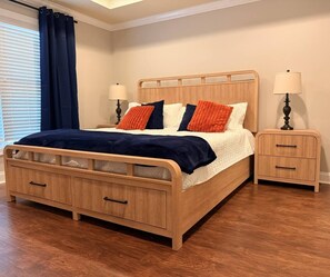 Een houten bed met opbergladen, twee nachtkastjes met lampen en een raam met gordijnen.
