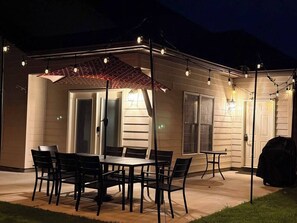 Un patio exterior con mesa y sillas, un espacio de estar cubierto y una parrilla.