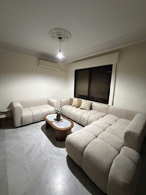A living room with a sectional sofa, a coffee table, and a ceiling light. - 3-bedroom apartment prime location (Amman)