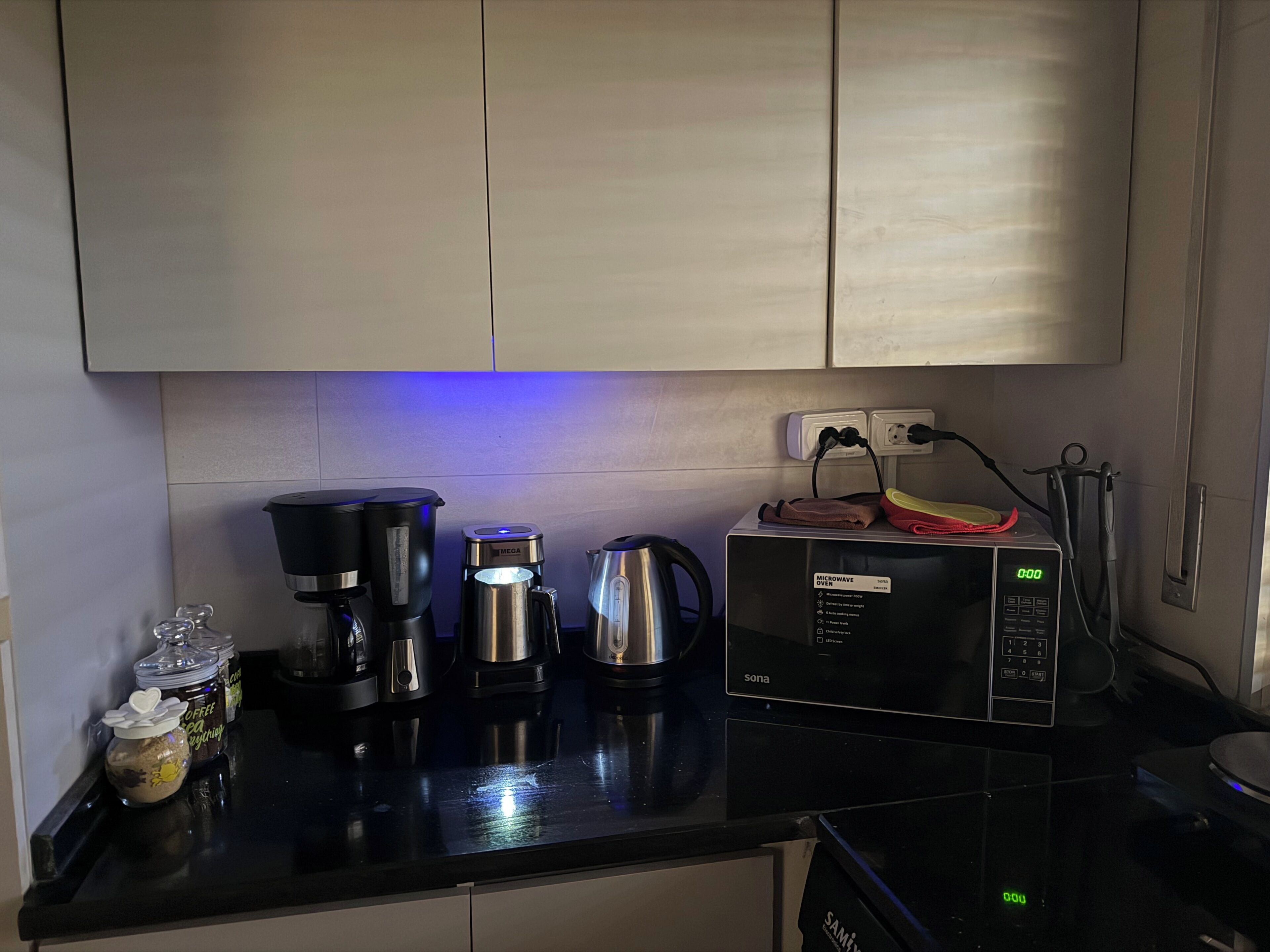 Una cocina con microondas, cafetera, hervidor y tarros de café.