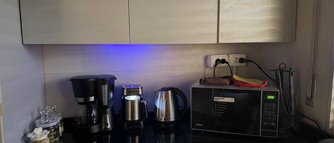 A kitchen with a microwave, coffee maker, kettle, and jars of coffee.
