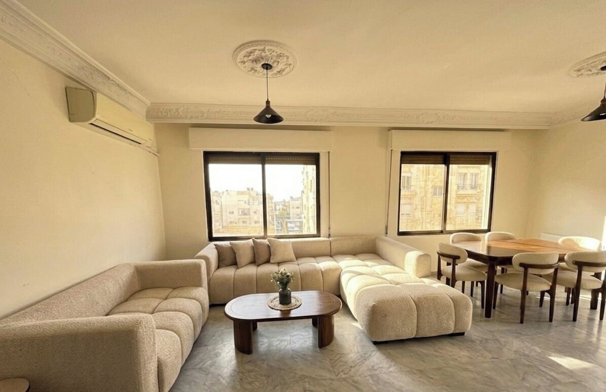 Una sala de estar con un sofá modular, una mesa de centro redonda y un comedor con mesa y sillas.