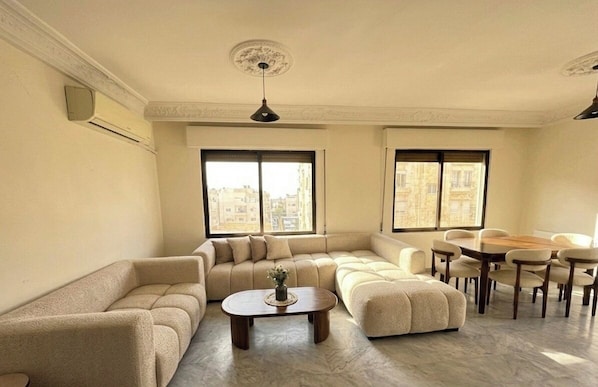 A living room with a sectional sofa, a round coffee table, and a dining area with a table and chairs. - 3-bedroom apartment prime location (Amman)