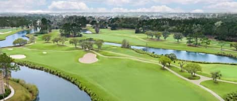 A golf course with water hazards, sand bunkers, and a clear sky.