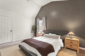 Un dormitorio con cama, mesitas de noche, lámpara, planta y ventana con cortinas.