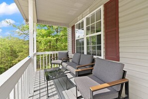 A covered porch with a seating area, a glass table, and a view of greenery. - RRG Peaceful Escape: Hot Tub, Game Room, Sleeps 16 (Stanton)