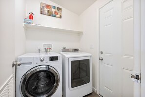 A laundry room with a front-loading washer and dryer, a fire extinguisher, and a shelf with a first aid kit. - West Sedona Retreat - Near Trails & Red Rocks (Sedona)
