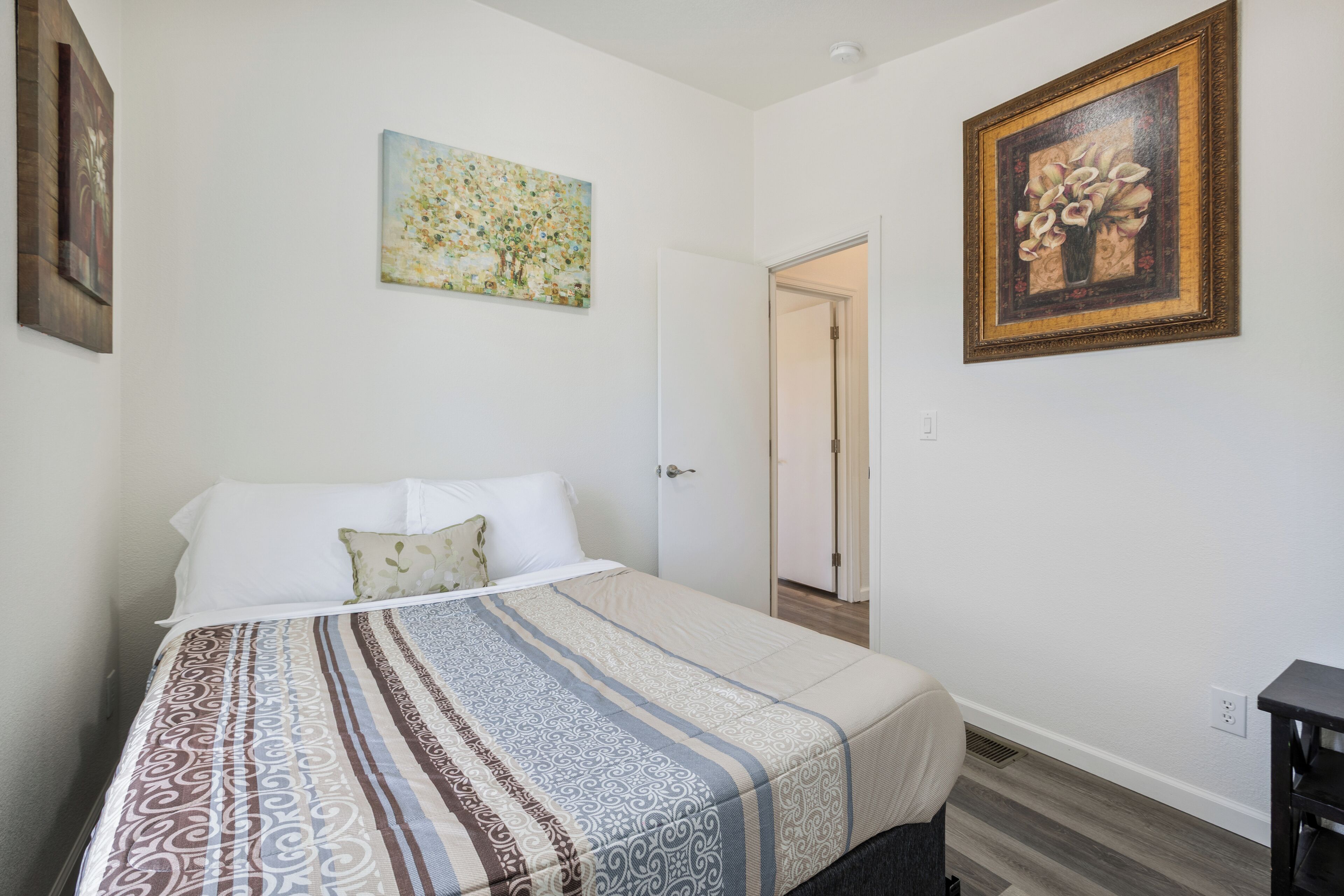 A bedroom with a bed, a door, and two framed artworks on the walls.