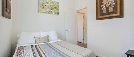 A bedroom with a bed, a door, and two framed artworks on the walls.