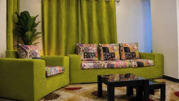 A green sofa with floral cushions, a black coffee table, and a large plant in a corner.