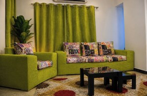 A green sofa with floral cushions, a black coffee table, and a large plant in a corner.
