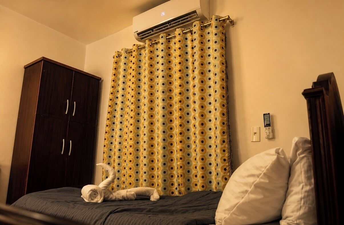 Ett hotellrum med en säng, en garderob, en gardin och en väggmonterad luftkonditioneringsanläggning.