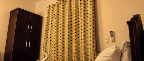 A hotel room with a bed, a wardrobe, a curtain, and a wall-mounted air conditioner.