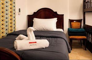 A hotel room with a bed, a chair, a bedside table, and a wall-mounted telephone.
