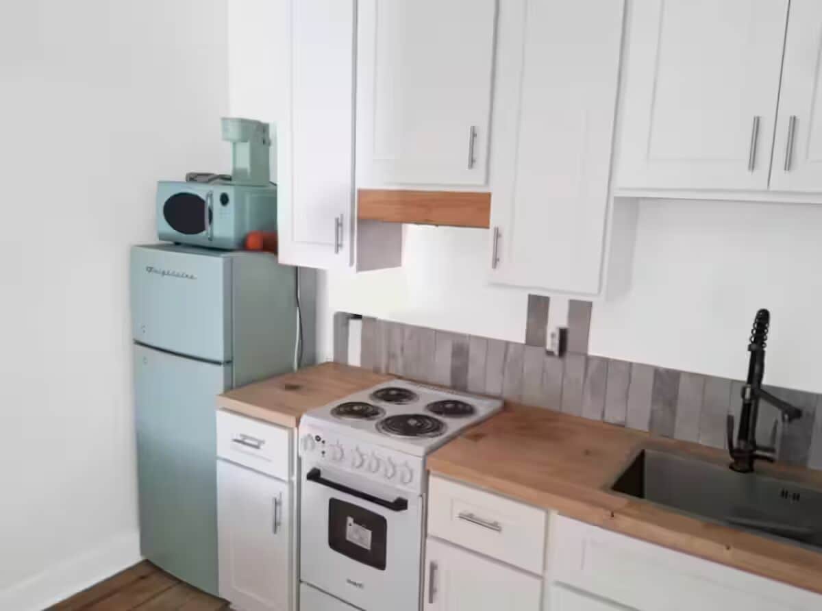 A compact kitchen with white cabinets, a wooden countertop, a built-in stove, and a sink.