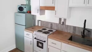 A compact kitchen with white cabinets, a wooden countertop, a built-in stove, and a sink.