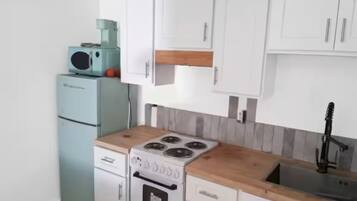 A compact kitchen with white cabinets, a wooden countertop, a built-in stove, and a sink.