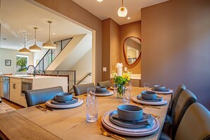 A dining area with a long table set for four, a kitchen in the background, and a staircase leading to another level. - River Street Lookout- Lux 3BD w/ Rooftop Views + Hot tub Downtown Hailey (Hailey)