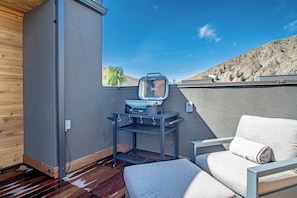 Un espacio de estar compacto al aire libre con una parrilla y una ventana con vistas a un paisaje montañoso.