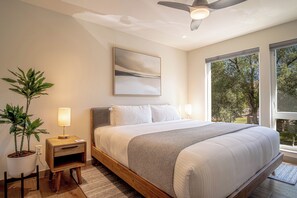 A bedroom with a bed, bedside tables, a ceiling fan, a window with a view of trees, and a painting on the wall. - River Street Lookout- Lux 3BD w/ Rooftop Views + Hot tub Downtown Hailey (Hailey)