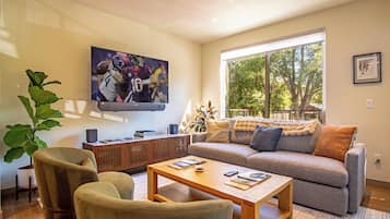 Una sala de estar moderna con un televisor de pantalla plana, un sofá, una mesa de centro y un ventanal grande.