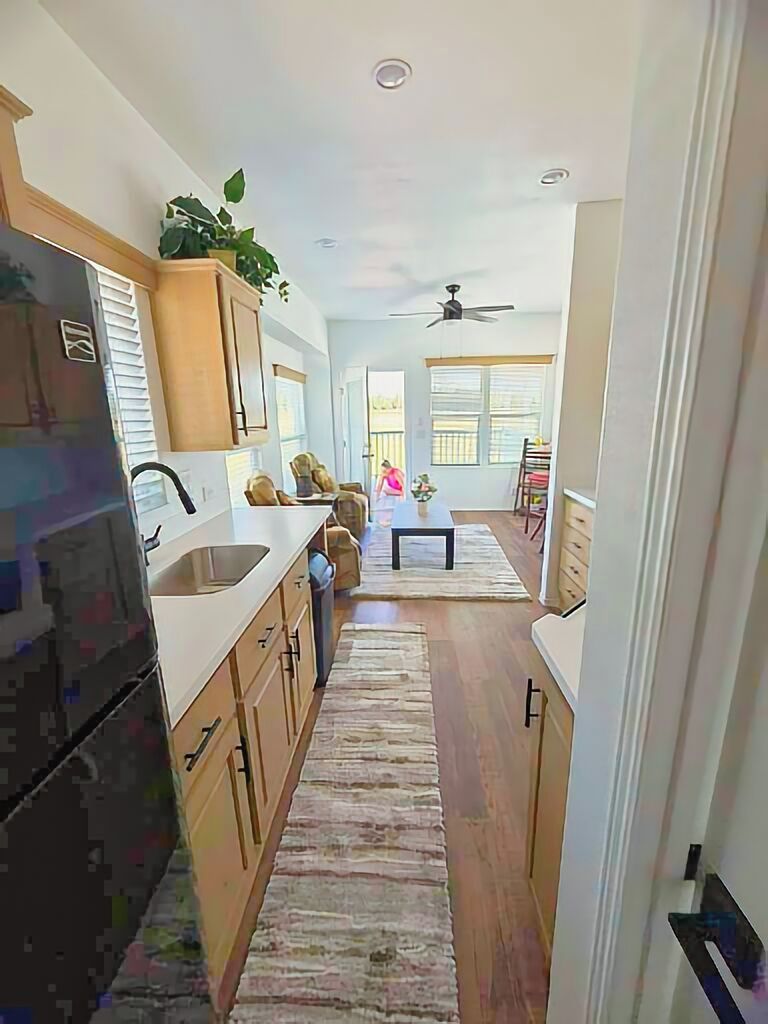 A narrow kitchen with wooden cabinets, a refrigerator, and a dining area with a table and chairs.
