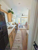 A narrow kitchen with wooden cabinets, a refrigerator, and a dining area with a table and chairs.