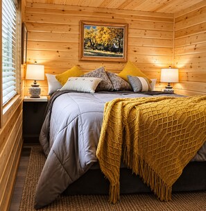 A cozy bedroom with a bed, pillows, a blanket, and a painting on the wall.