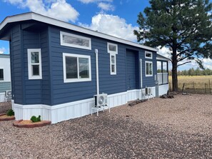A single-story blue house with white trim, a small porch, and a gravel driveway.