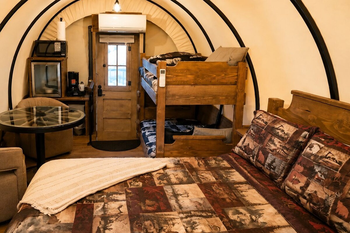 A compact room with a bunk bed, a small table with a chair, a microwave, and a coffee machine.