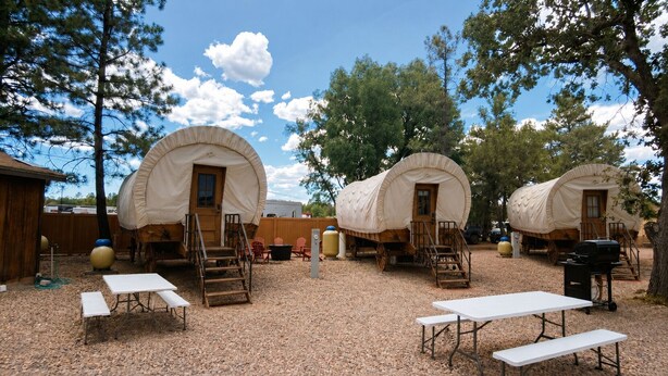 Un camping con carros cubiertos, mesas de picnic y una parrilla.