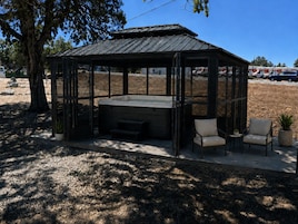 Un espacio de estar al aire libre techado con un jacuzzi, dos sillones y una mesita.