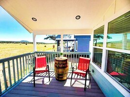 Un porche cubierto con vistas a un campo, dos sillas rojas y un barril de madera.