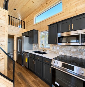A modern kitchen with black cabinets, stainless steel appliances, and a stone backsplash.