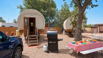 A campsite with covered structures, a barbecue grill, and a picnic table with food.