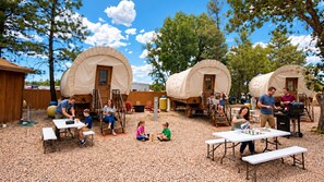 A campsite with covered wagons, picnic tables, and people engaging in various activities.