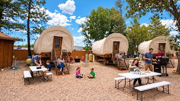 A campsite with covered wagons, picnic tables, and people engaging in various activities.
