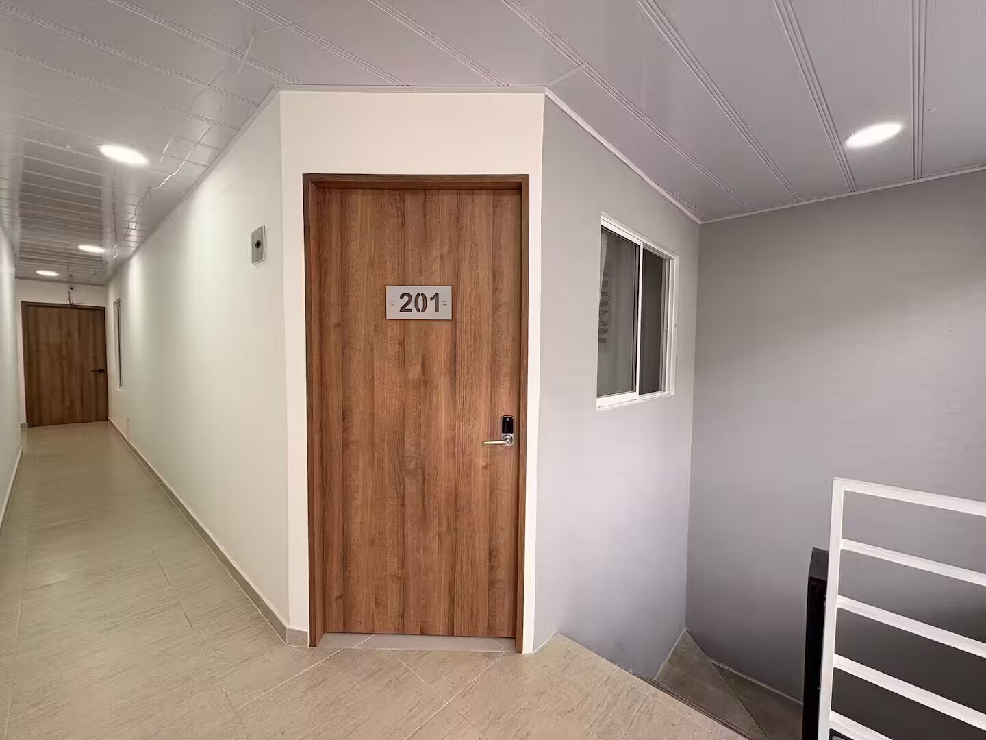 A hallway with a wooden door labeled '201' and a window on the adjacent wall.
