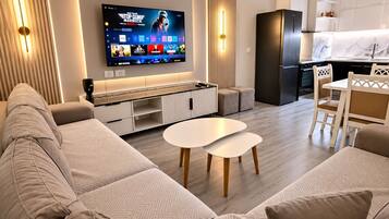 Un soggiorno moderno con un'ampia TV a schermo piatto, un divano, un tavolino da caffè e un'area pranzo con sedie.