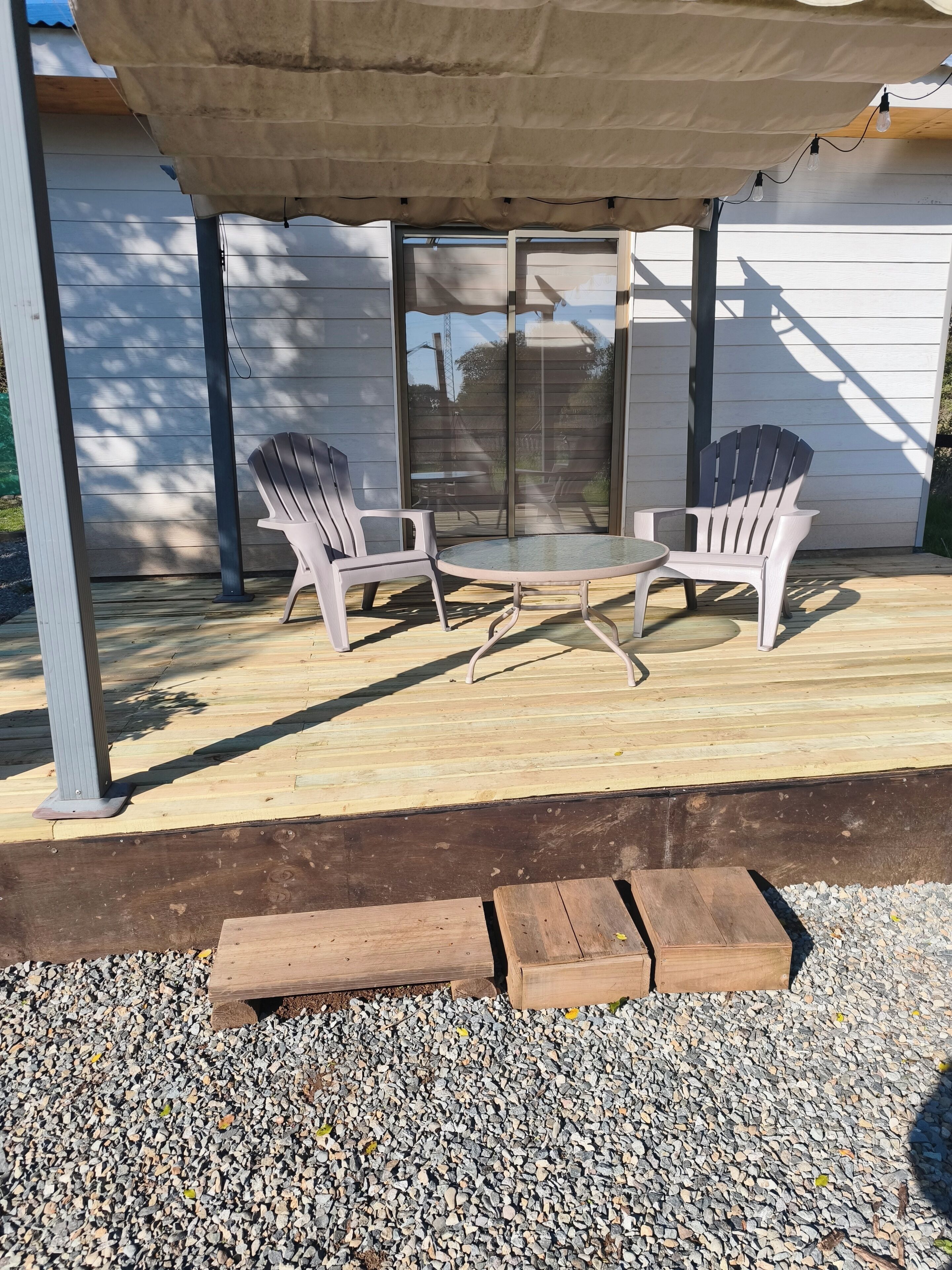 Une terrasse extérieure avec des fauteuils Adirondack, une table en verre et un banc en bois.