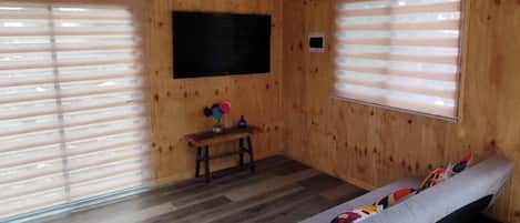 A wooden cabin room with a bed, a small table with a vase, and a TV mounted on the wall.