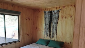 A wooden room with a bed, a window, and a curtain.