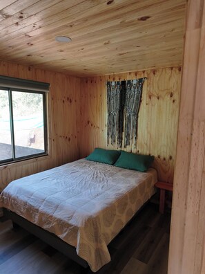 A wooden room with a bed, a window, and a curtain.